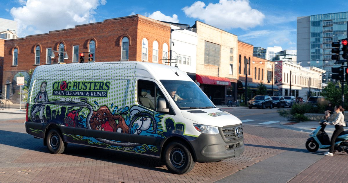 A wrapped Clog Busters drain cleaning van parked on a downtown street
